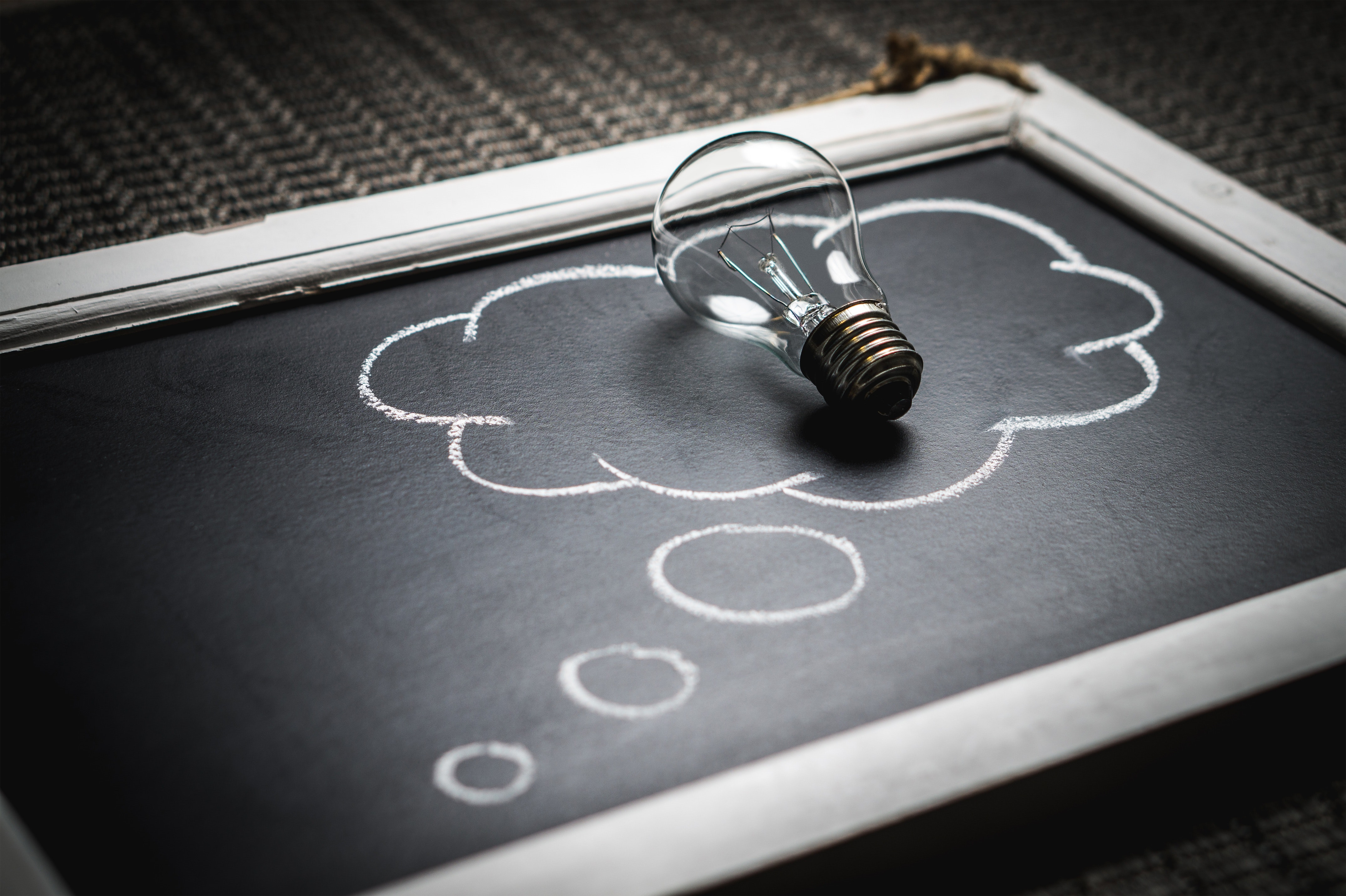 Image of a light bulb on top of a chalkboard with a drawing of cloud representing an idea